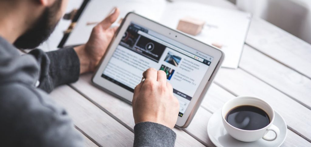 A man who is working with his iPad and a coffee next to him