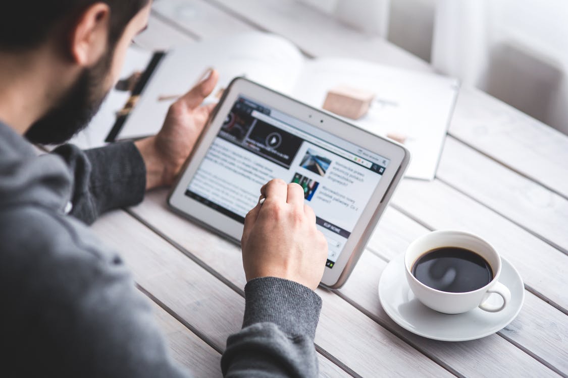 A man who is working with his iPad and a coffee next to him