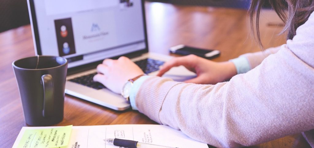 Eine Frau, die an einem Tisch mit Laptop, Kaffee, Handy und Notizbuch sitzt