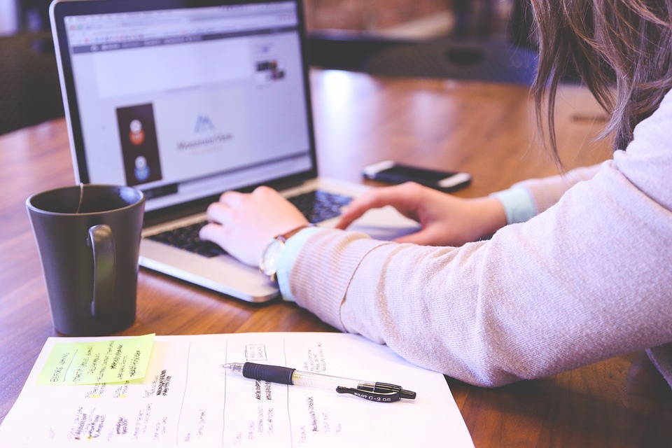 Eine Frau, die an einem Tisch mit Laptop, Kaffee, Handy und Notizbuch sitzt